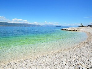 Een kiezelstrand met helder water en verre bergen.