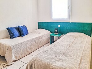 Ein Zimmer mit zwei Betten, einem kleinen Tisch mit Lampe und einem Fenster.