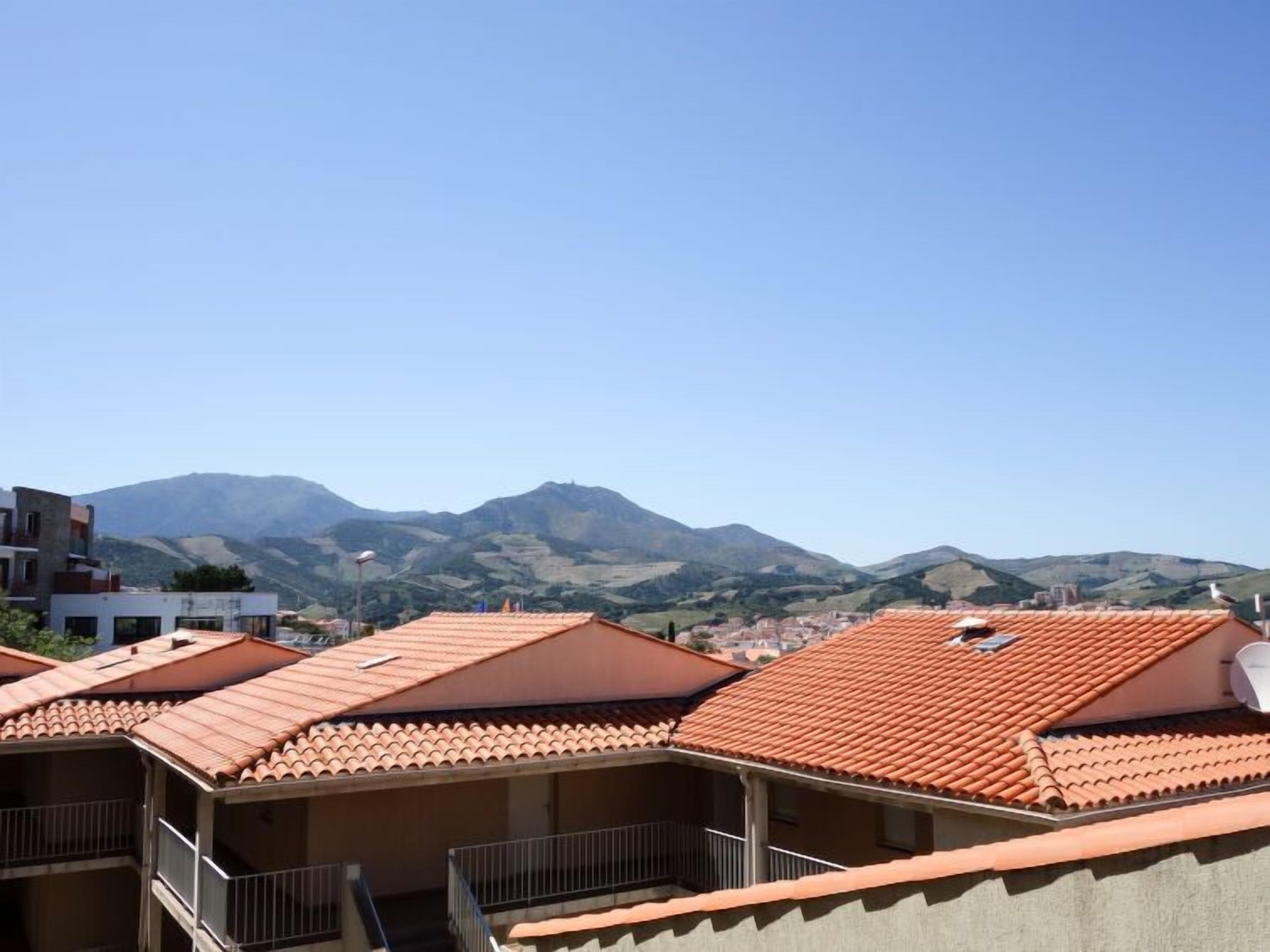 A residential area with terracotta-tiled roofs and a mountainous backdrop.