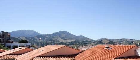 A residential area with terracotta-tiled roofs and a mountainous backdrop.