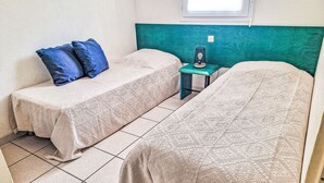 Una habitación con dos camas, una mesita y una ventana.