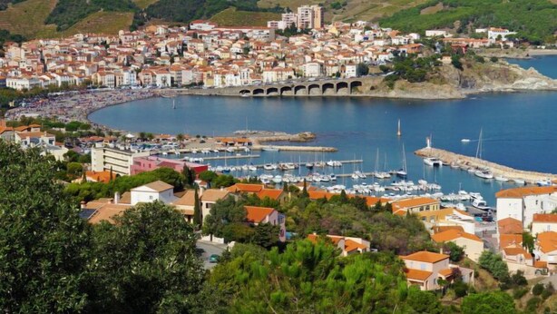 Un pueblo costero con un puerto deportivo, edificios de techo rojo y un puente que lo conecta con el continente.