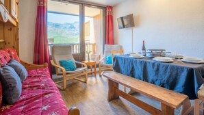 A cozy room with a bed, a bench, a table set for dining, and a TV on the wall. - Roche Blanche 183 by Interhome (Val Thorens)