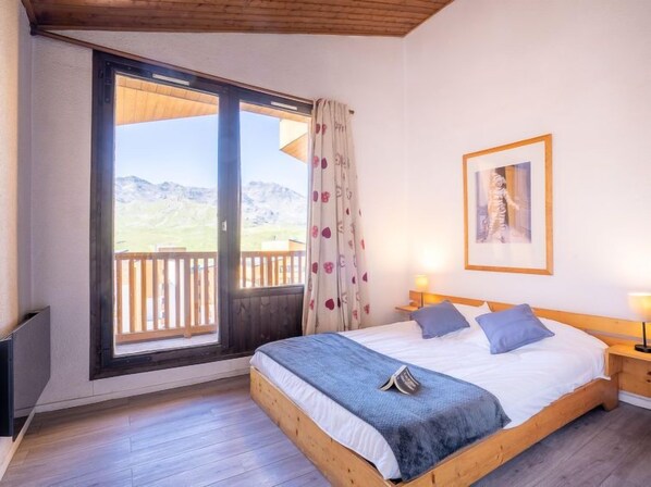 Een slaapkamer met een houten bed, een groot raam met uitzicht op bergen en een lijst met een afbeelding aan de muur.