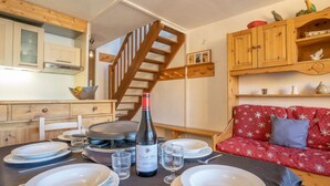 A dining area with a table set for four, a bottle of wine, and a staircase leading to an upper level. - Roche Blanche 183 by Interhome (Val Thorens)