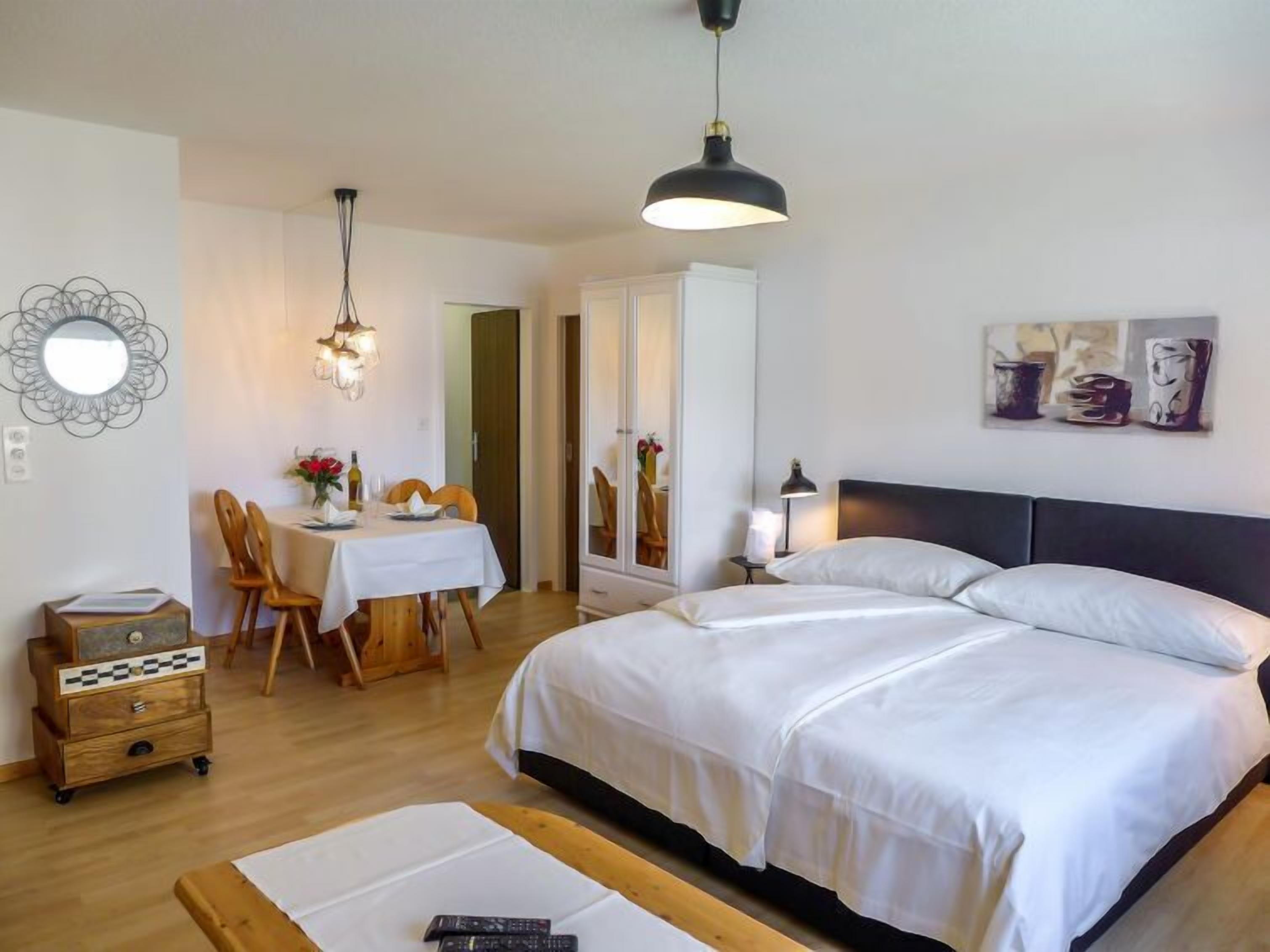 Une chambre à coucher avec un grand lit, une table à manger avec des chaises, un miroir et des œuvres d’art accrochées au mur.