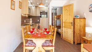 Een gezellig eetgedeelte met een houten tafel en stoelen, een keuken op de achtergrond en een stapelbed aan de rechterkant.
