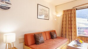 Een gezellige kamer met een houten bank, een kleine tafel met een fruitschaal, een lamp en een lijst met een afbeelding aan de muur.