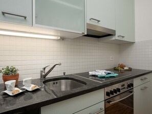 A modern kitchen with a stainless steel sink, white cabinets, a built-in oven, and a countertop with a potted plant and a plate of cookies.