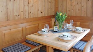 Un coin repas en bois avec une table dressée pour quatre personnes, comprenant des verres à vin, des assiettes et un vase avec des fleurs.