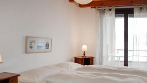 Une chambre d’hôtel avec un lit, une table de chevet avec une lampe, un tableau encadré au mur et une fenêtre avec des rideaux.