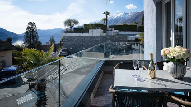 A balcony with a table set for two, overlooking a mountainous landscape and a body of water. - Suite Classic by Interhome (Ascona)
