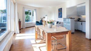A modern apartment with a dining area, kitchen, and a large window offering a view of the outdoors. - Suite Classic by Interhome (Ascona)