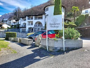 Letrero de 'Residenza Miralago' con vista a un edificio y un coche rojo al frente.