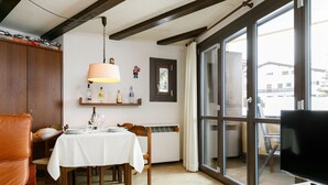 A dining area with a table set for two, a hanging lamp, and a television on a wooden stand. - Residenza Chesa Margun 34-7 by Interhome (Silvaplana-Surlej)
