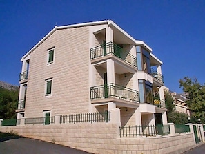 Un immeuble à plusieurs étages doté de balcons, d’une façade en briques et d’une entrée fermée par un portail.