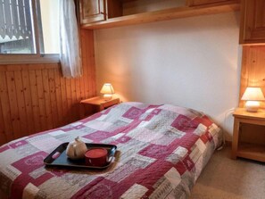 A cozy room with a wooden bed, a quilt, a tray with a candle and a teapot, and two bedside lamps.