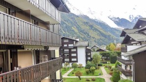 Un edificio de estilo chalé con balcón de madera, rodeado de un jardín cuidado y con montañas al fondo.