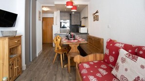 Un espai habitable compacte amb zona de menjador, petita cuina i un sofà vermell amb dibuixos.