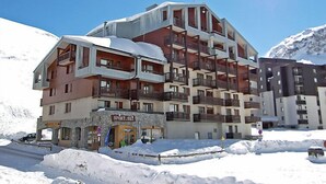Un hotel de diverses plantes amb balcons, un senyal de neu i un paisatge de muntanyes al fons.