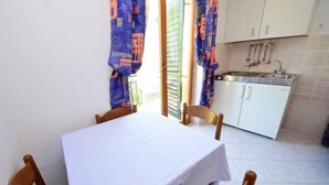 Un petit coin repas avec une table et des chaises, une cuisine équipée de placards et d’un évier, et des rideaux à motifs.