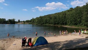 Ein Strand mit einem Zelt, Personen beim Schwimmen und einem bewaldeten Hintergrund.