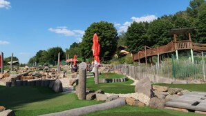 Ein rustikaler Außenbereich mit Holzbauten, einer Holzbrücke und einem Rasenfeld.