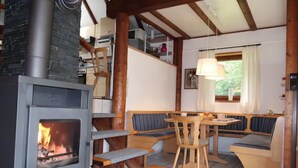 Ein gemütlicher Raum mit Kamin, Holzbänken, einem Esstisch und einem mit Vorhängen versehenen Fenster.
