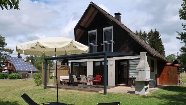 Ein Haus mit überdachter Terrasse, Gartenmöbeln und Schornstein.