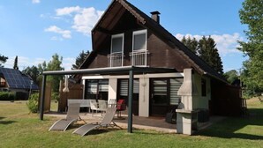 Ein zweistöckiges Haus mit Balkon, einer überdachten Terrasse mit Stühlen und einem Solarmodul im Hintergrund.