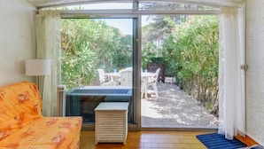 A room with a sliding glass door leading to a garden. There is a sofa and a small table in the room. - Résidence Green Village 2 by Interhome (Cap d'Agde)