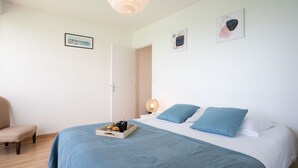 A bedroom with a bed, a chair, and a bedside table with a lamp. - Bellevue by Interhome (Quiberon)