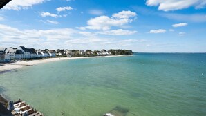 A coastal view with clear turquoise waters, a sandy beach, and a row of white buildings with a dock extending into the water. - Bellevue by Interhome (Quiberon)