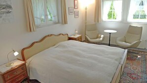 Een hotelkamer met een groot bed, twee stoelen, een tafeltje en een vloerlamp.