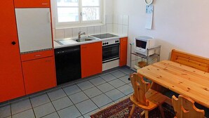 Een kleine keuken met een spoelbak, fornuis en magnetron, een eettafel met stoelen, en een raam met uitzicht.