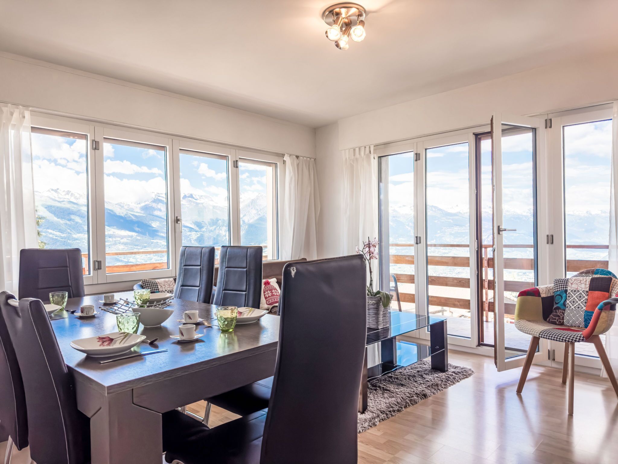Ein Essbereich mit einem Tisch für vier Personen, großen Fenstern mit Bergblick und einem Balkon mit Holzgeländer.