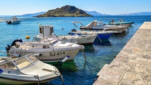 Un port de plaisance où sont amarrés plusieurs bateaux, une jetée en pierre et une île qui se profile à l’horizon.
