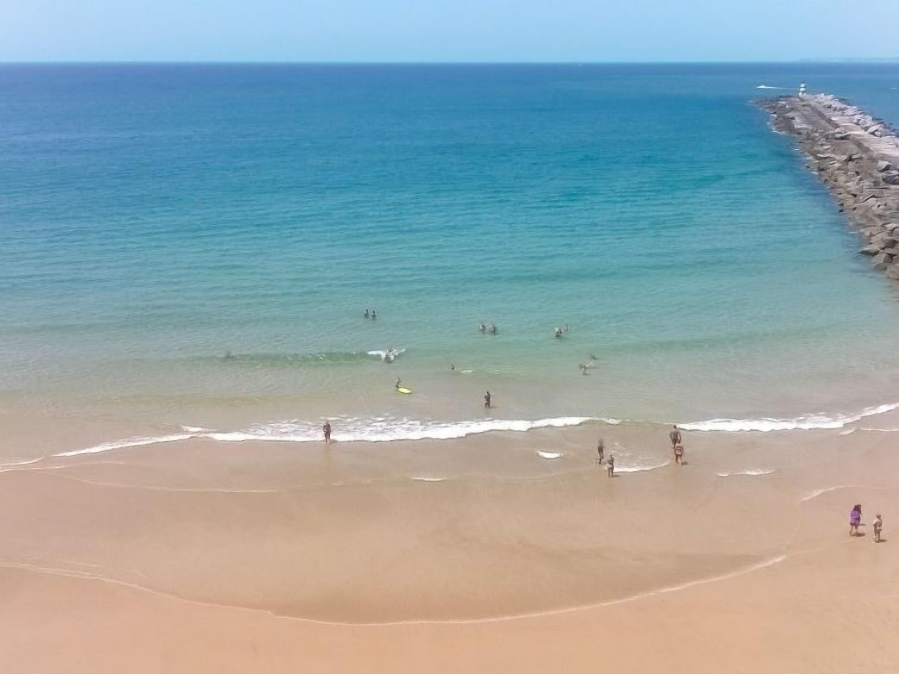 Une plage où l’on voit des gens se baigner et se promener le long du rivage.