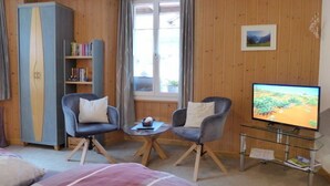A cozy room with a bed, two armchairs, a small table, a TV, a bookshelf, and a window with curtains. - Apartment Rösli by Interhome (Lauterbrunnen)