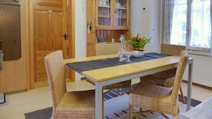A dining area with a wooden table and wicker chairs, a cabinet with glass doors, and a window with curtains. - Apartment Rösli by Interhome (Lauterbrunnen)