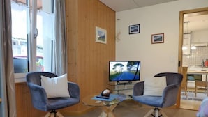 A cozy room with two armchairs, a small coffee table, and a television displaying a scenic road. - Apartment Rösli by Interhome (Lauterbrunnen)