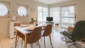 Een eethoek met een tafel voor vier personen, stoelen, een televisie en een bank.
