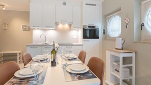 Een moderne keuken met witte kasten, een inbouwoven en een eethoek voor zes personen, met een witte tafel en bruine stoelen.