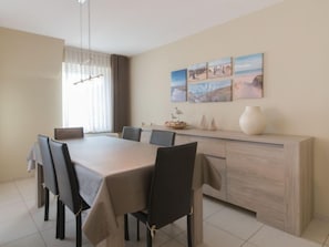 A dining area with a long table, chairs, a light-colored cabinet, and a window with curtains.