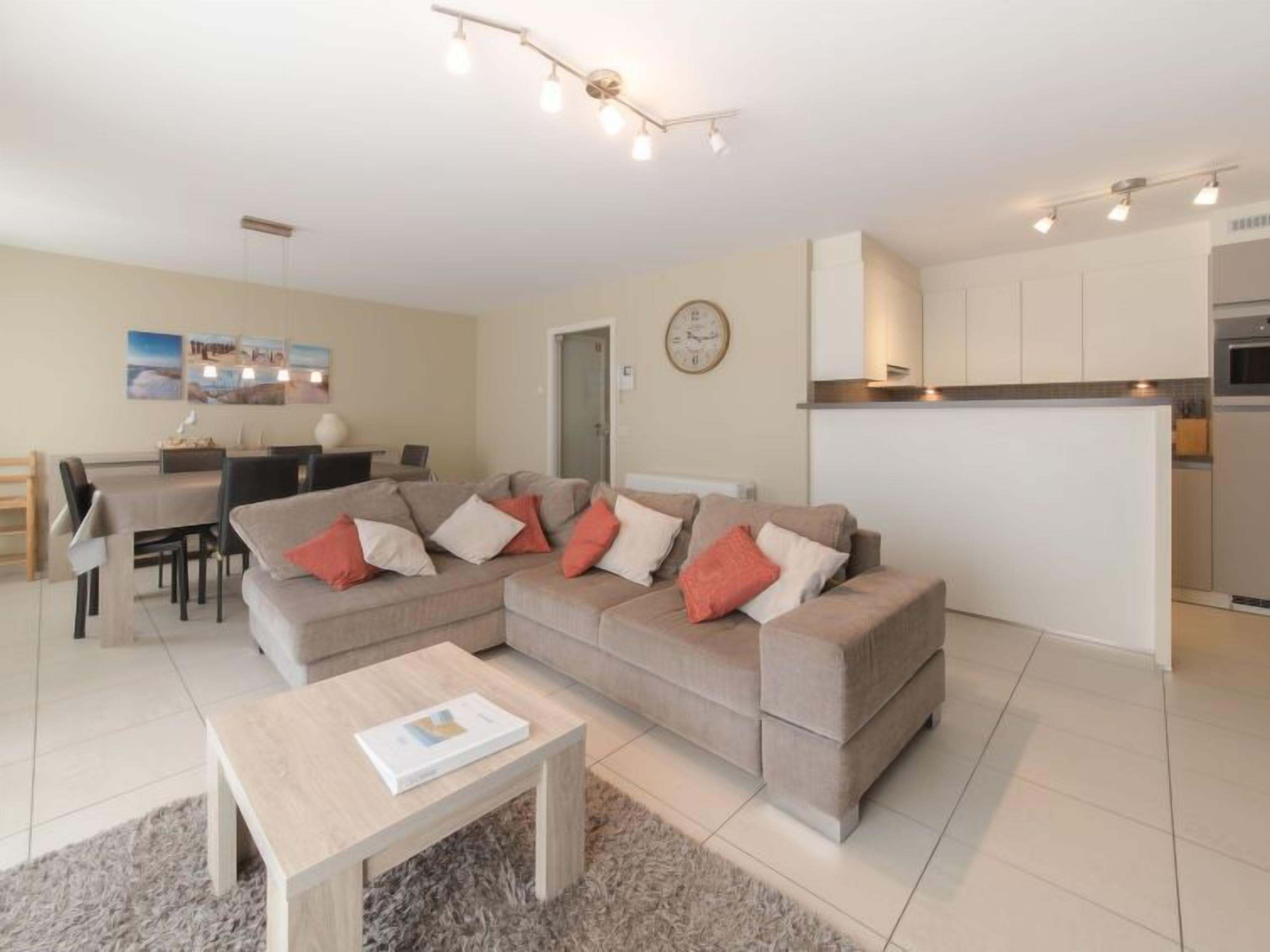 Un salon moderne avec un canapé d’angle beige, une table basse et un coin repas comprenant une table et des chaises.