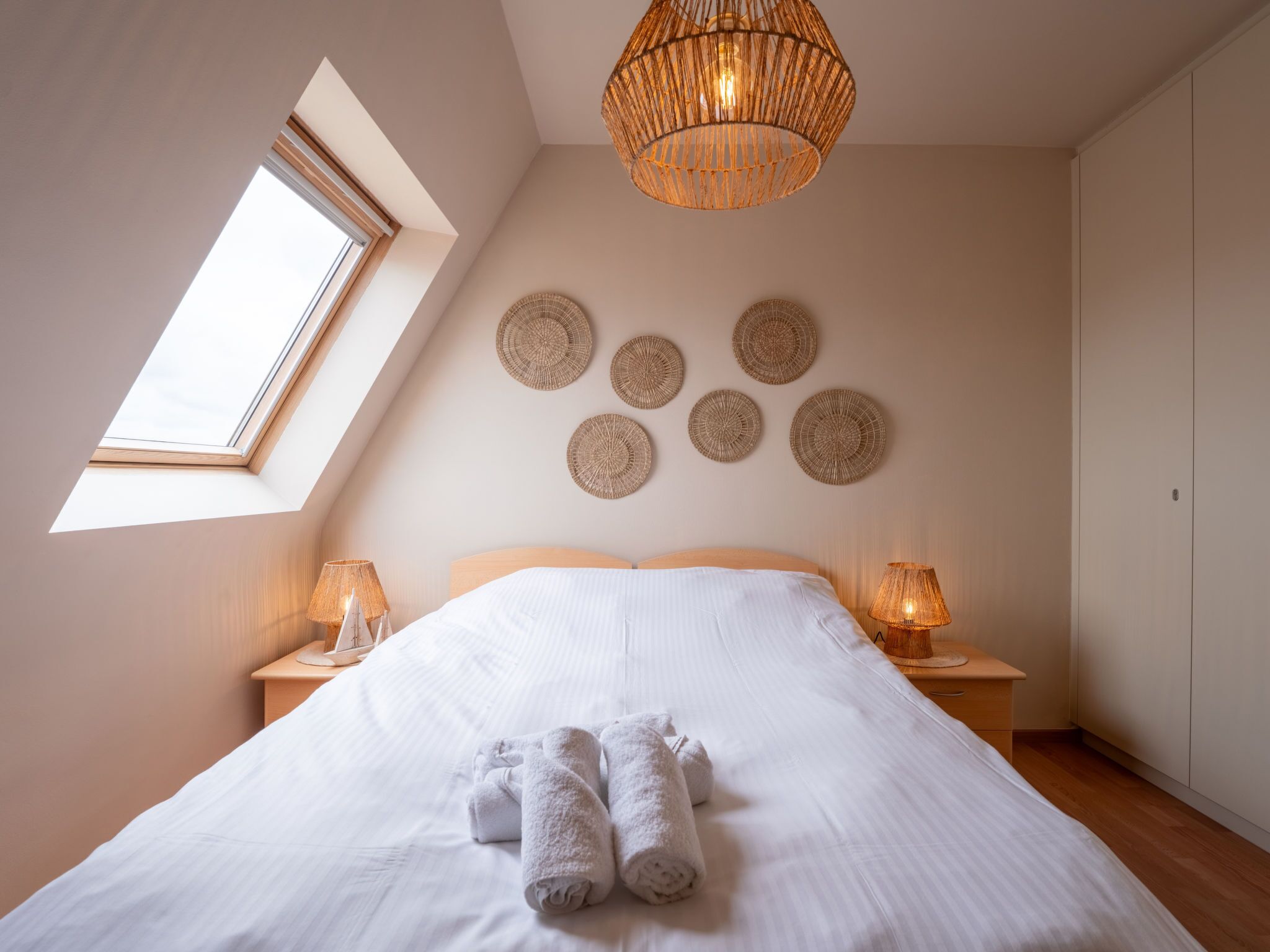 A bedroom with a large bed, two bedside lamps, a skylight, and a woven ceiling light fixture.