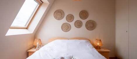 A bedroom with a large bed, two bedside lamps, a skylight, and a woven ceiling light fixture.