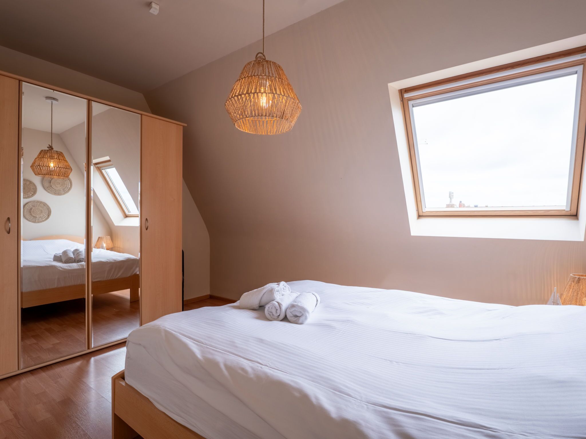 Ein Schlafzimmer mit Bett, Kleiderschrank, Pendelleuchte und Fenster.