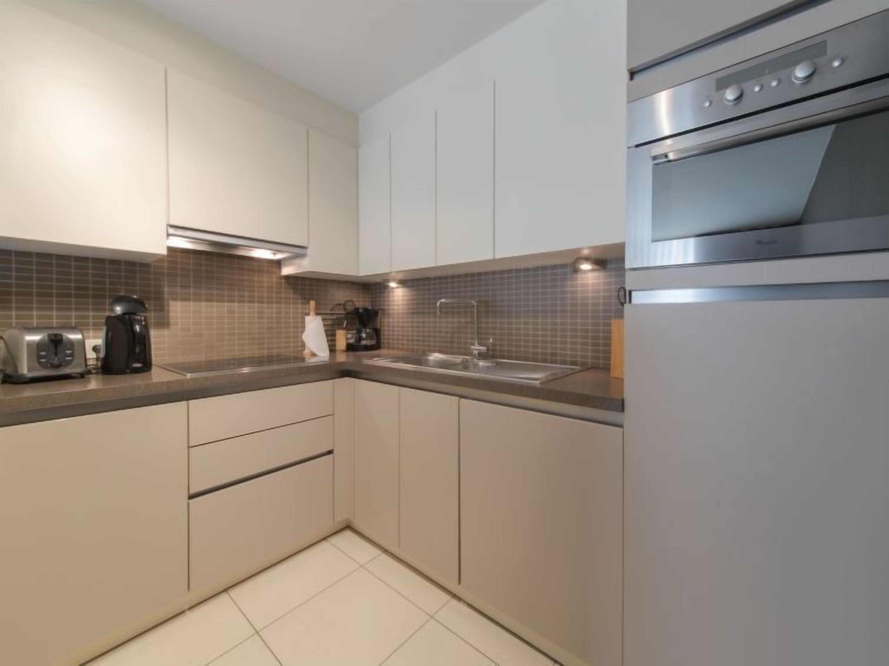 Eine moderne Küche mit weißen Schränken, einem Edelstahlbackofen, einer Kaffeemaschine und einem Toaster.