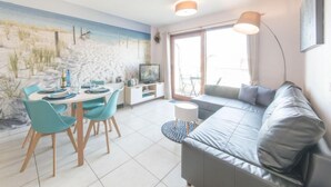 Een moderne woonkamer met een grijze bank, turquoise stoelen, een eettafel en een muurschildering met een strandthema.